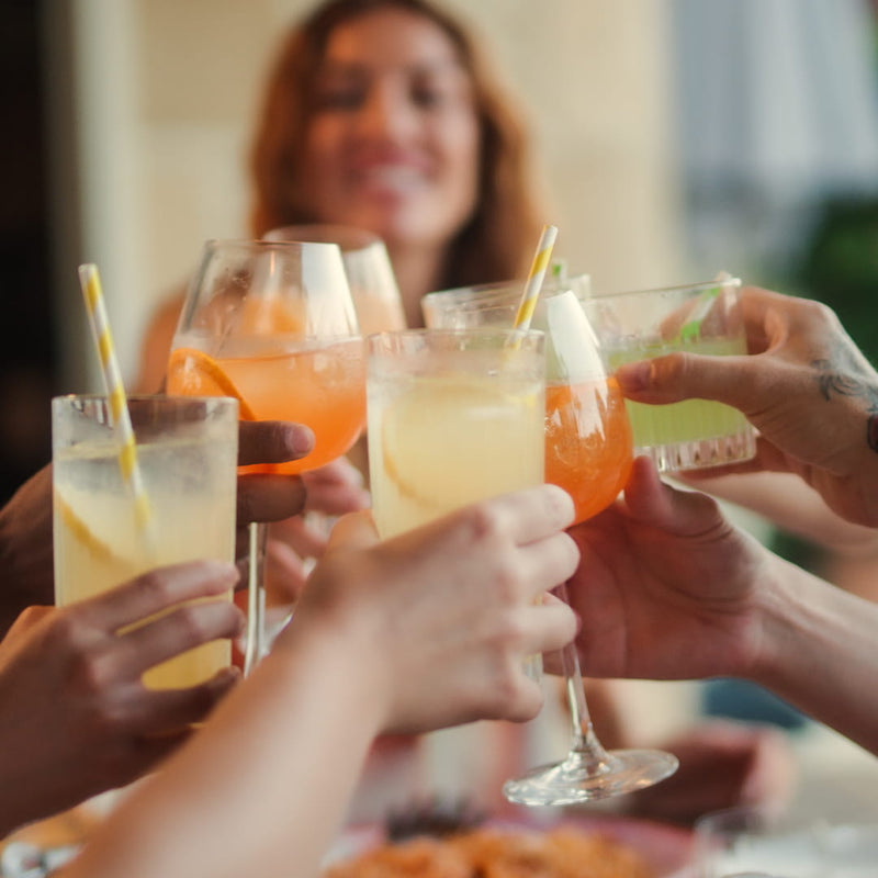 Freunde stoßen gemeinsam mit fruchtigen LOLA Aperitif-Drinks in Orange, Lemon und Lime an.