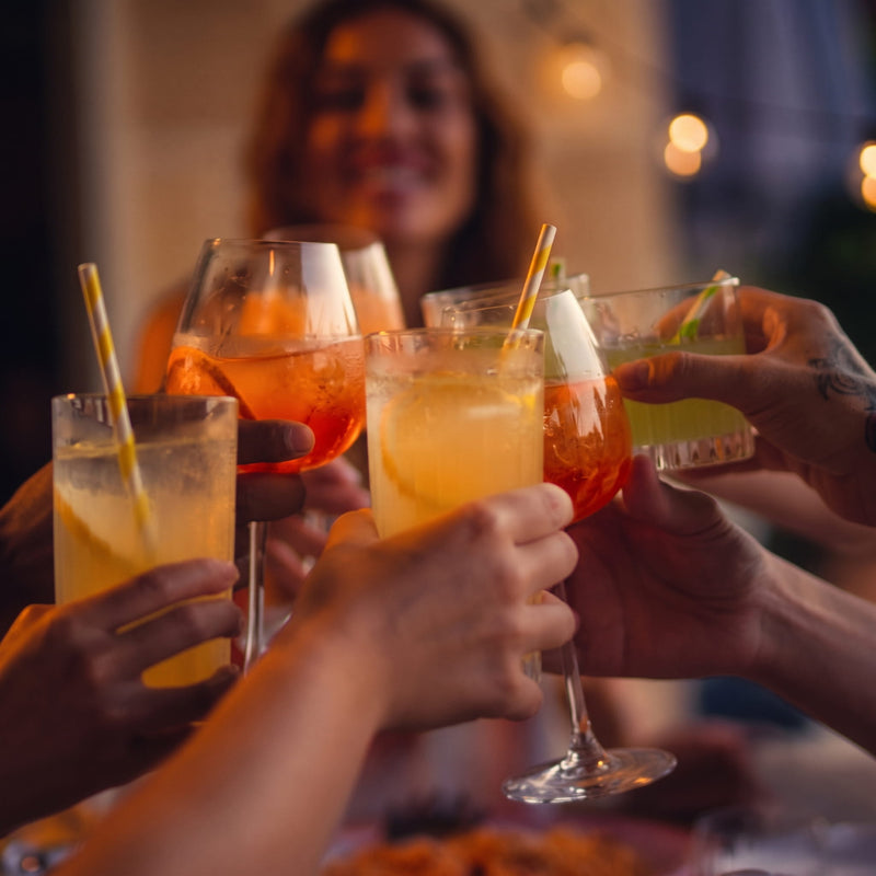 Freunde stoßen gemeinsam mit fruchtigen LOLA Aperitif-Drinks in Orange, Lemon und Lime an.