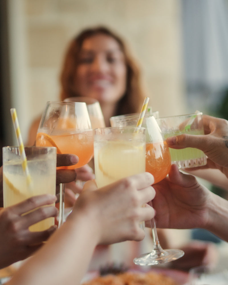 Freunde stoßen mit bunten Aperitif-Drinks an und genießen gemeinsam einen sommerlichen LOLA Moment.