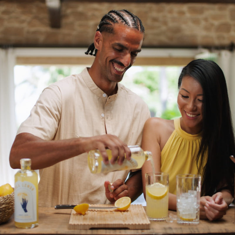 Ein Mann bereitet gemeinsam mit einer Frau einen LOLA LEMON Aperitif-Drink mit frischer Zitrone zu.