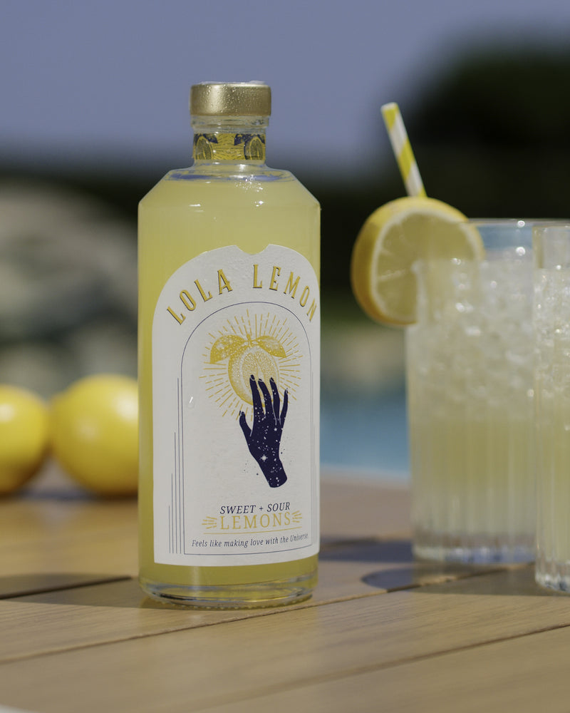LOLA LEMON Aperitif-Flasche neben einem eisgekühlten Zitronendrink mit frischer Zitronenscheibe.