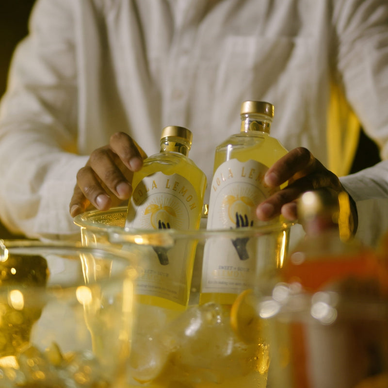 Ein Mann bereitet gemeinsam mit einer Frau einen LOLA LEMON Aperitif-Drink mit frischer Zitrone zu.
