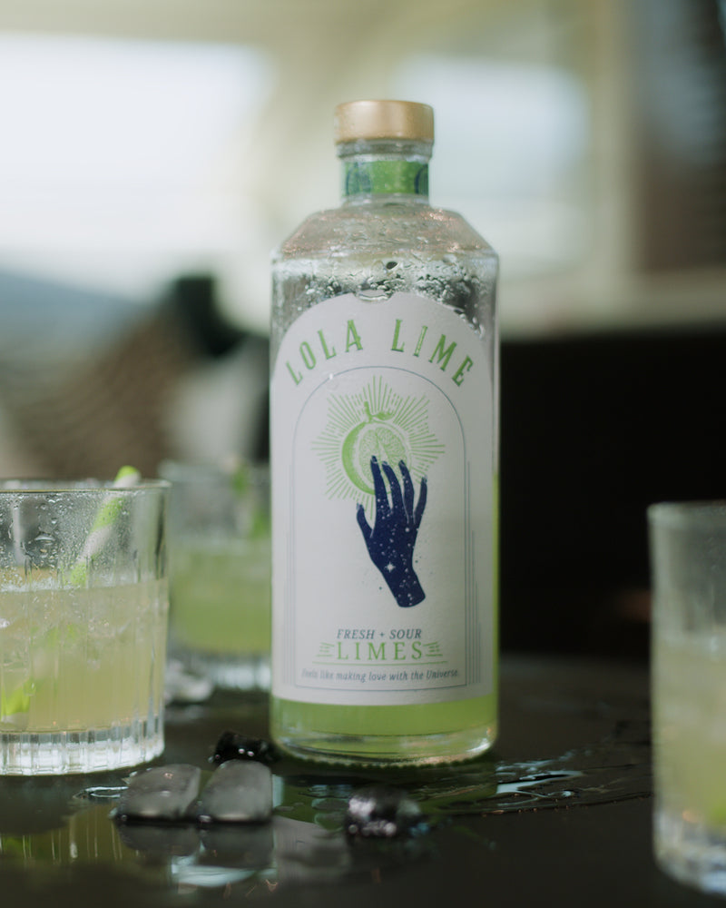 LOLA LIME Aperitif-Flasche mit eisgekühlten Limetten-Drinks und frischen Limetten in sommerlicher Atmosphäre.