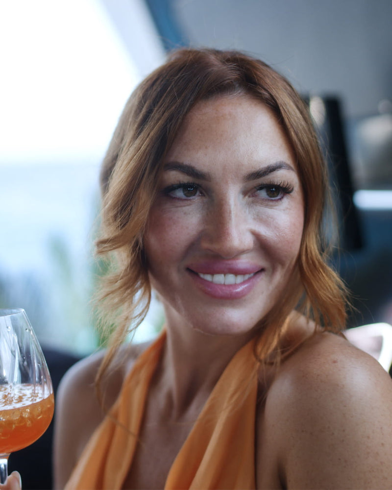 LOLA ORANGE Aperitif-Flasche mit eisgekühltem Orange-Drink und frischen Orangen in sommerlicher Atmosphäre.